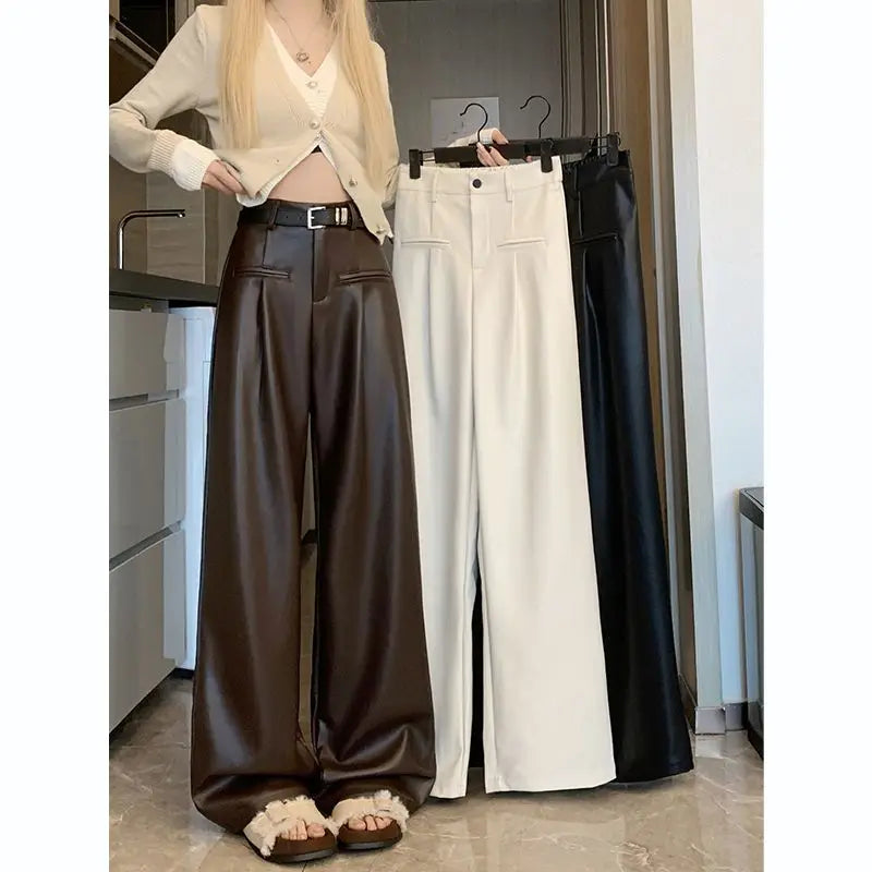 Model in brown faux leather wide-leg pants holding black and cream pairs on a hanger, front view