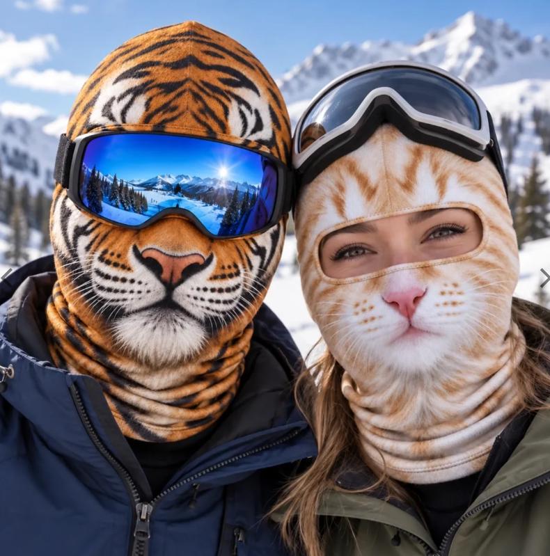 May include: Two balaclavas featuring realistic animal prints. One balaclava displays a tiger face with orange, black, and white stripes, worn with blue-tinted ski goggles. The other balaclava shows a ginger cat face, worn with black ski goggles.