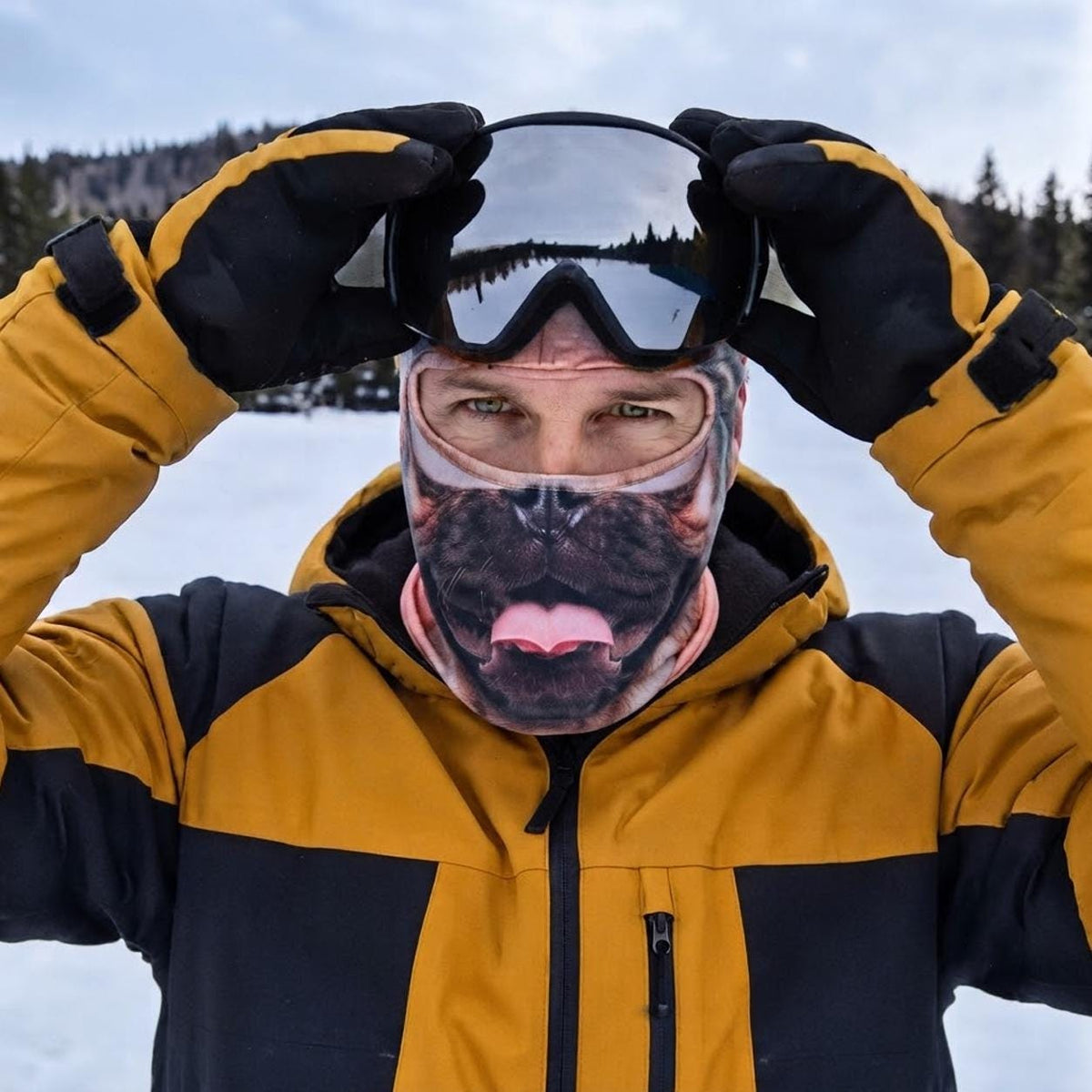 May include: A face mask featuring a realistic pug dog print with a pink tongue, worn under black ski goggles with a reflective lens. The attire includes a mustard yellow and black hooded winter jacket and black insulated gloves for cold weather.