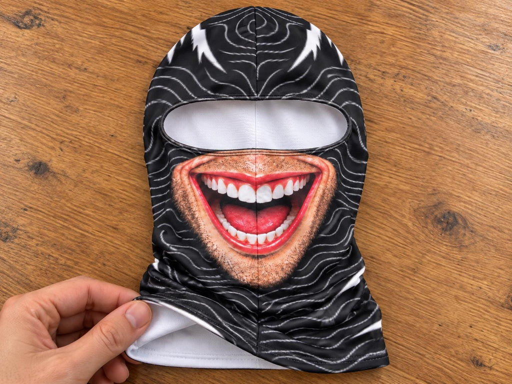 May include: A black balaclava featuring a white wavy line pattern and a realistic graphic print of a wide, laughing mouth with white teeth, red lips, and light stubble. The headgear has a single horizontal eye opening and a white interior lining.