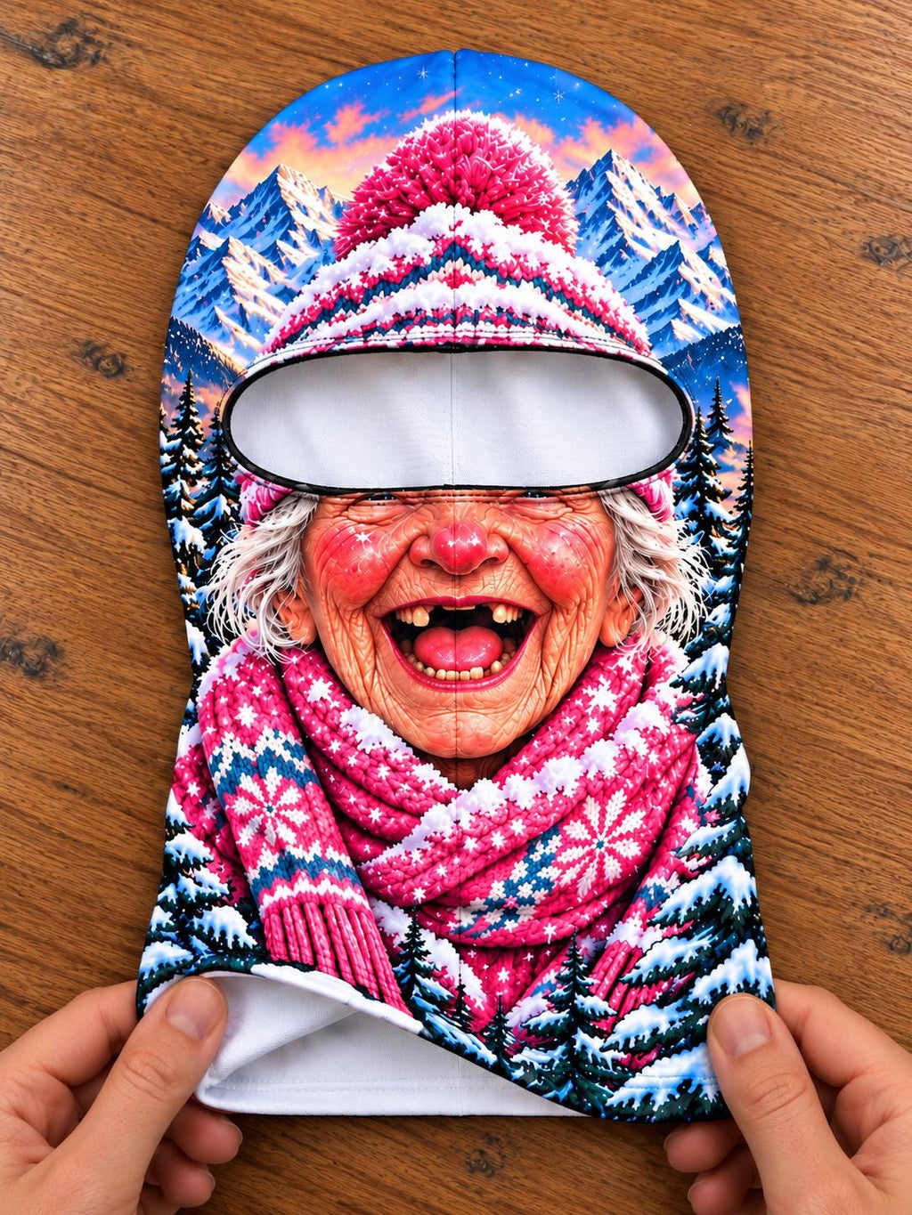 May include: A balaclava featuring a vibrant, full-color graphic print of an elderly person with rosy cheeks and a wide, toothless smile. The person wears a pink knit-style hat with a pom-pom and a matching pink patterned scarf against a snowy mountain.