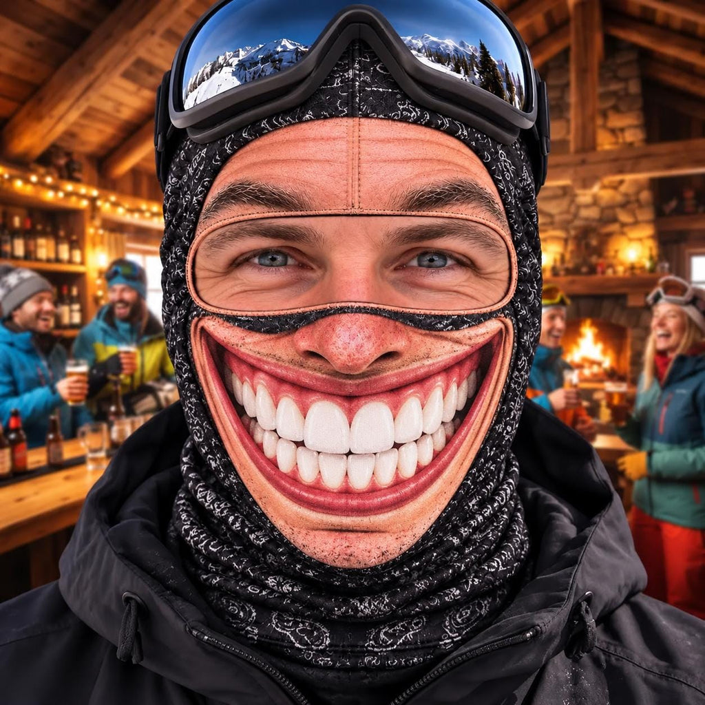 May include: A black balaclava featuring a printed graphic of a wide, toothy grin across the mouth area. The headgear is made of a dark fabric with a subtle white pattern and is worn with a pair of dark-tinted ski goggles resting on the forehead.